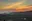 a group of people sitting on a cliff looking at a sunset